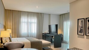 A hotel room with a bed, a desk with a television, a chair, and two framed pictures on the wall. - Suite Manhattan by ¼ UmQuarto 10-PR. (Curitiba)