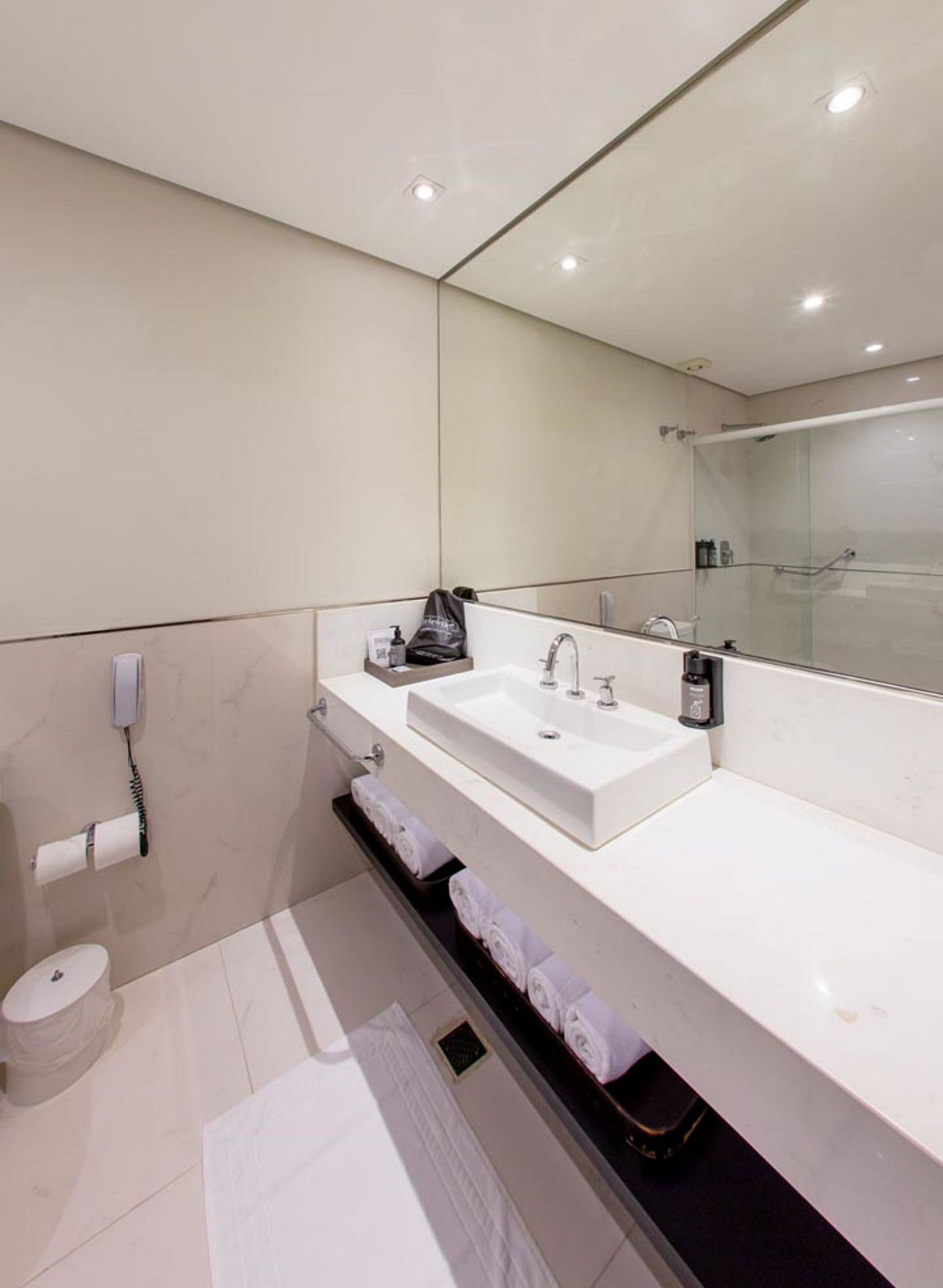 A modern bathroom with a large mirror, two sinks, a toilet, and a towel rack.