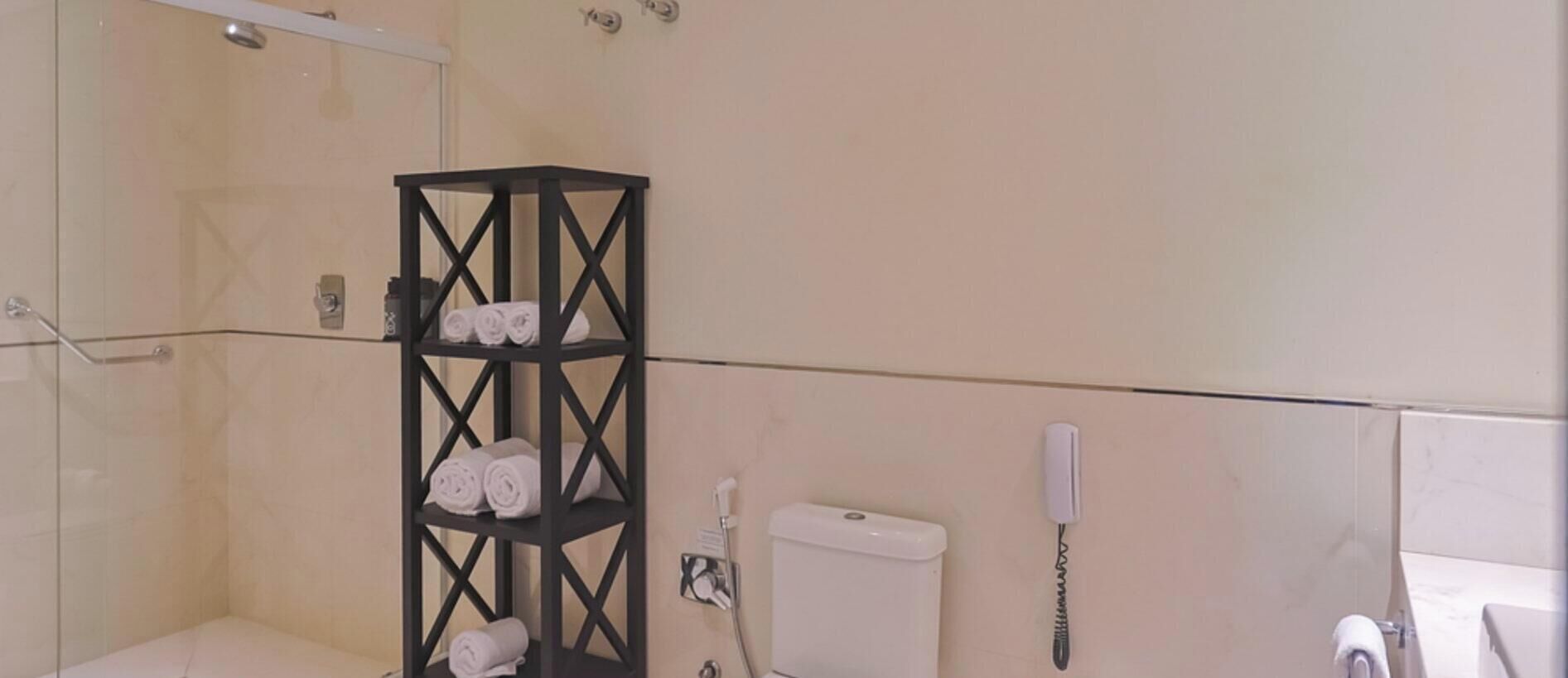 Een badkamer met een douchecabine van glas, een metalen plank in zwart met handdoeken, een toilet en een telefoon.