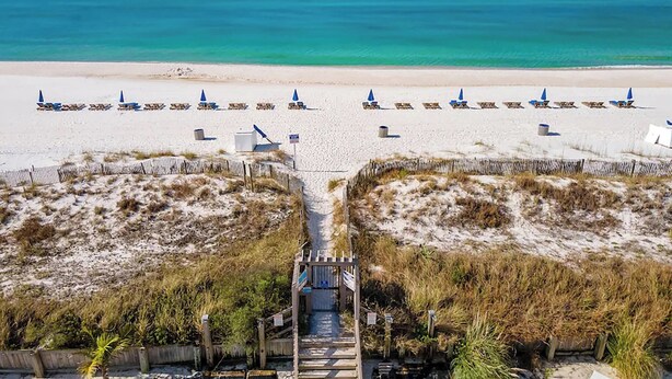 A beach with rows of sun loungers and umbrellas, a wooden pathway leading to the beach, and a clear view of the ocean.