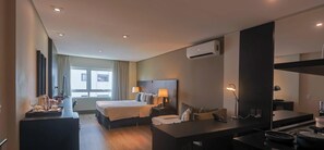 Habitació d'hotel amb llit, taules de nit, escriptori, aire condicionat i finestra amb cortines.