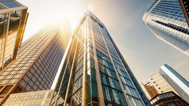 A tall glass building with a modern design, surrounded by other high-rise structures.