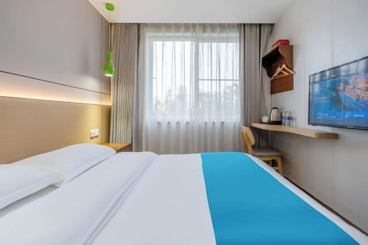 Una habitación de hotel con cama, televisor, ventana con cortinas y escritorio con silla.