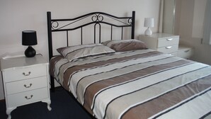 A neatly made bed with striped bedding, a black metal headboard, and a bedside table with a lamp.