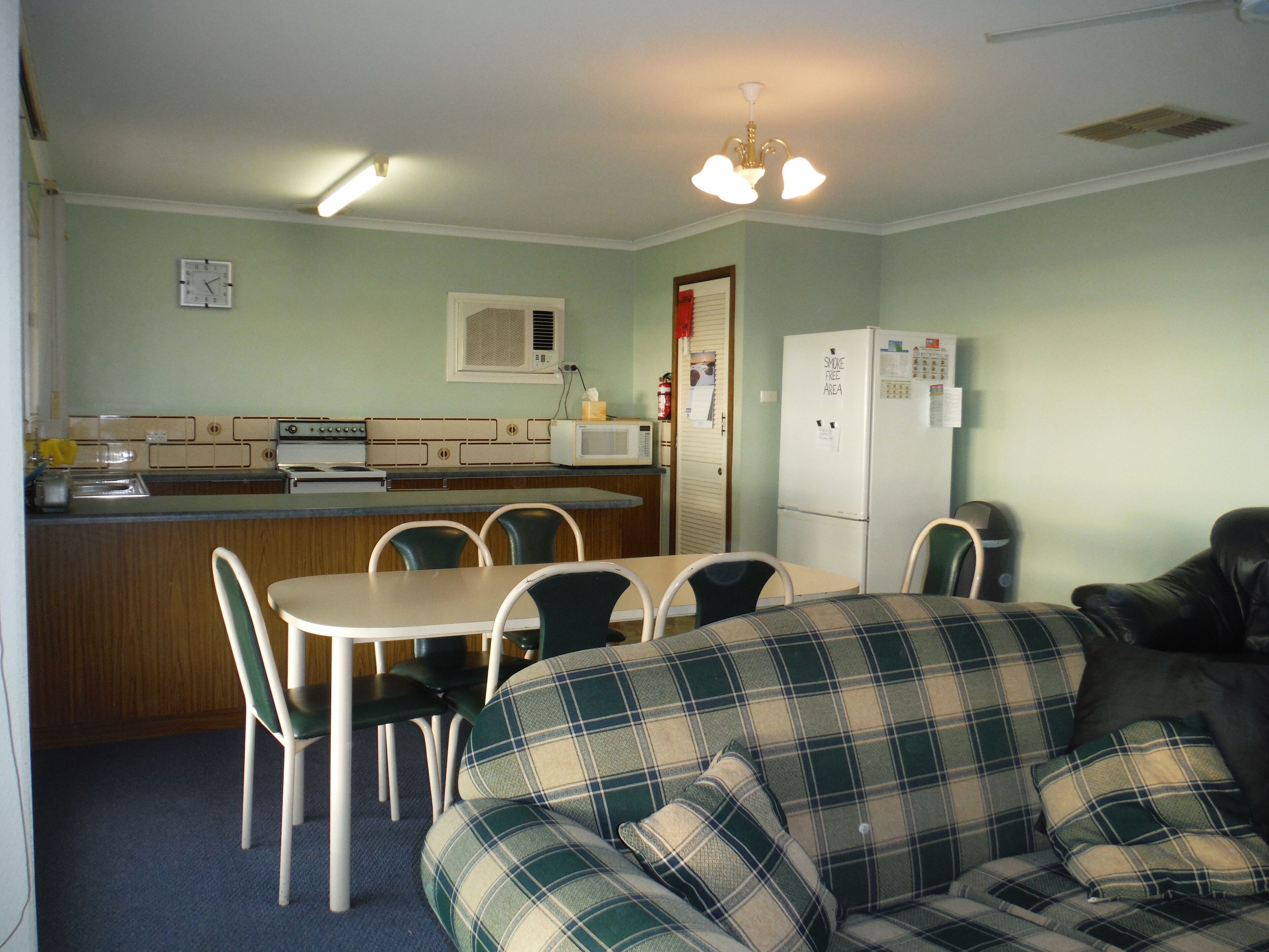 A compact kitchen with a microwave, stove, and refrigerator. There is a dining table with chairs and a plaid sofa.