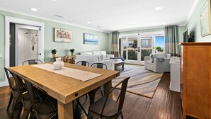 Un salon moderne comprenant un coin repas, un ensemble de canapés et une vue sur l’extérieur grâce à de grandes portes vitrées.