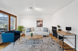 A modern living room with a sofa, a blue armchair, a coffee table, and a desk with a chair.