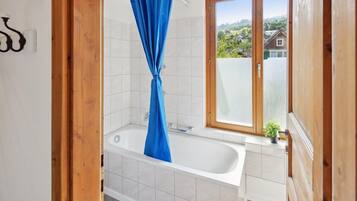 A bathroom with a bathtub, a shower curtain, and a window with a view of houses.