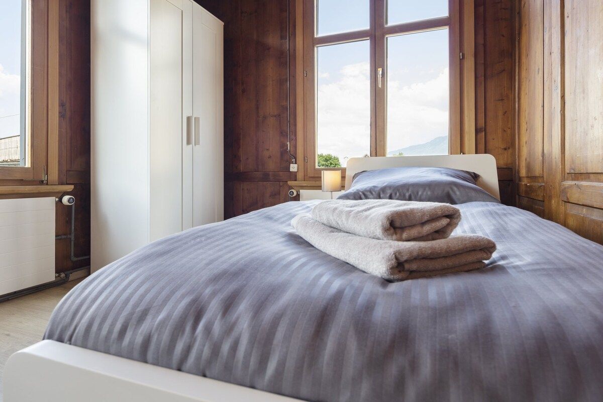 A bedroom with a large bed, wooden walls, a window, and a nightstand.