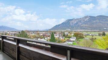 A view from a balcony overlooking a town with houses, trees, and mountains in the background.