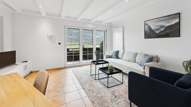 Un salon moderne avec un canapé, une table basse, un téléviseur et une grande fenêtre.