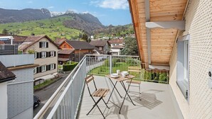 Un balcón con mesa y sillas, con vistas a una zona residencial con casas y montañas al fondo.