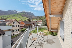 Un balcon avec une table et des chaises, donnant sur un quartier résidentiel avec des maisons et des montagnes en arrière-plan.