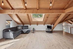 Un loft spacieux avec un plafond en bois, une lucarne, un canapé d’angle gris, une petite table et un téléviseur.