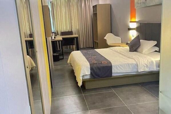 Una habitación de hotel con cama, escritorio, silla, armario y espejo.