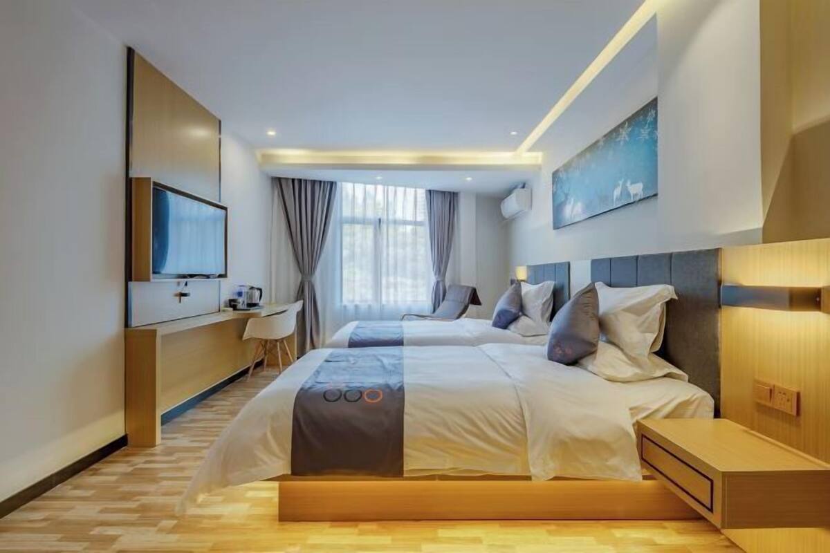 A modern hotel room with a bed, bedside tables, a desk, a flat-screen TV, and a window with curtains.