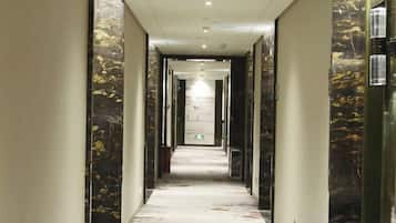 Un pasillo con paredes de mármol y suelo estampado, que conduce a una puerta al final.
