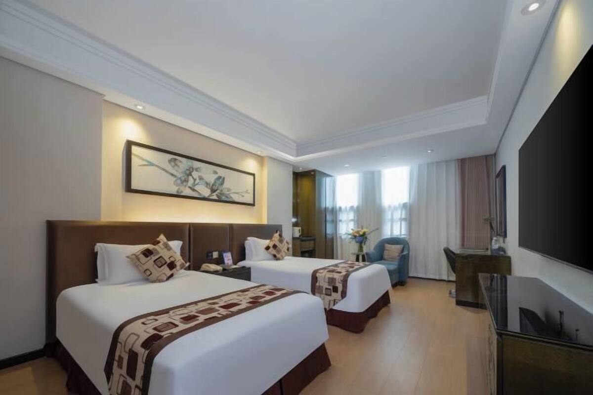 A hotel room with two beds, a flat-screen TV, a desk, and a large painting on the wall.