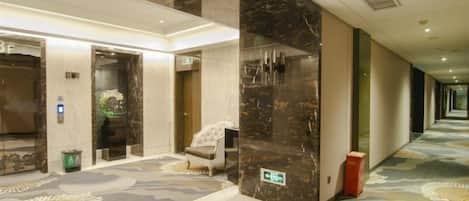 A hotel lobby with marble walls, a patterned carpet, and an elevator.