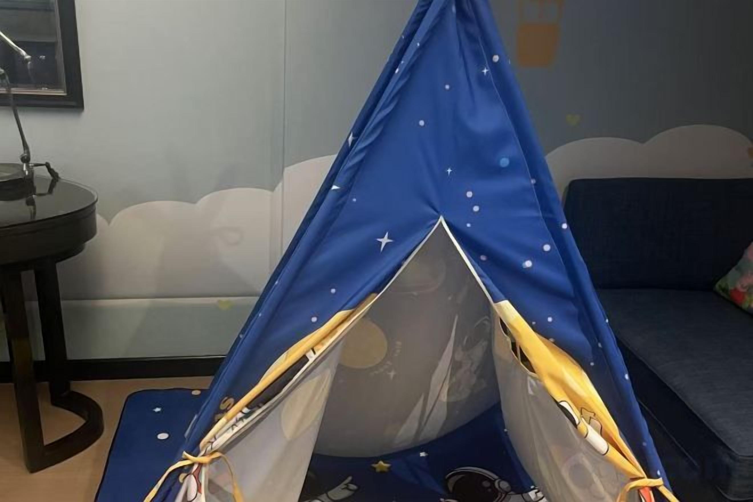 Una tenda blava amb estrelles i planetes estampats, muntada en una habitació amb un sofà i una taula petita.