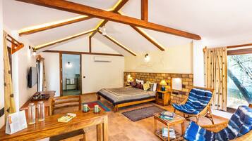 Une pièce spacieuse avec un plafond haut, des poutres en bois, un lit avec une tête de lit, deux fauteuils en osier, une petite table et une fenêtre avec des rideaux.
