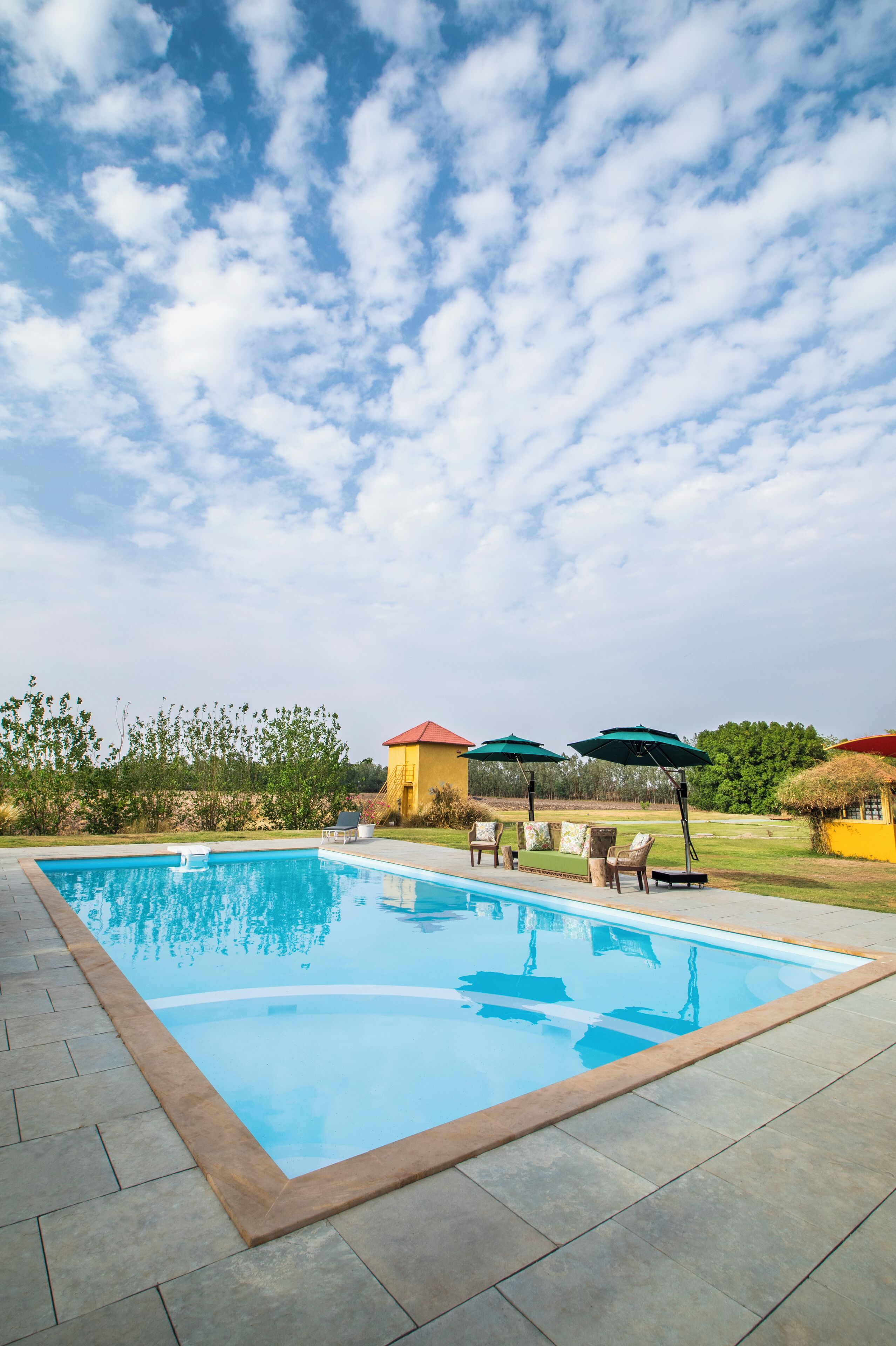 A swimming pool with a tiled deck, surrounded by lounge chairs and umbrellas, with a clear sky above.