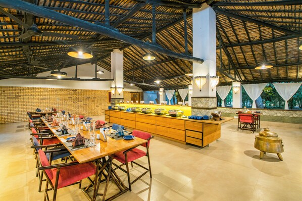 A spacious dining area with a long wooden table set for a meal, surrounded by colorful chairs. - Rann Riders (Dasada)