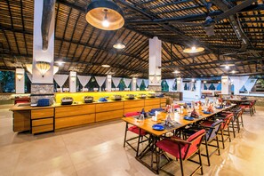A spacious dining area with a long wooden counter and multiple tables, each set with plates, glasses, and cutlery. - Rann Riders (Dasada)