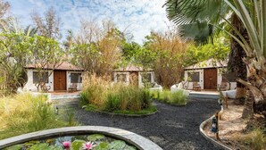 Un jardin paisible avec un étang, des palmiers et deux petites cabanes en bois.