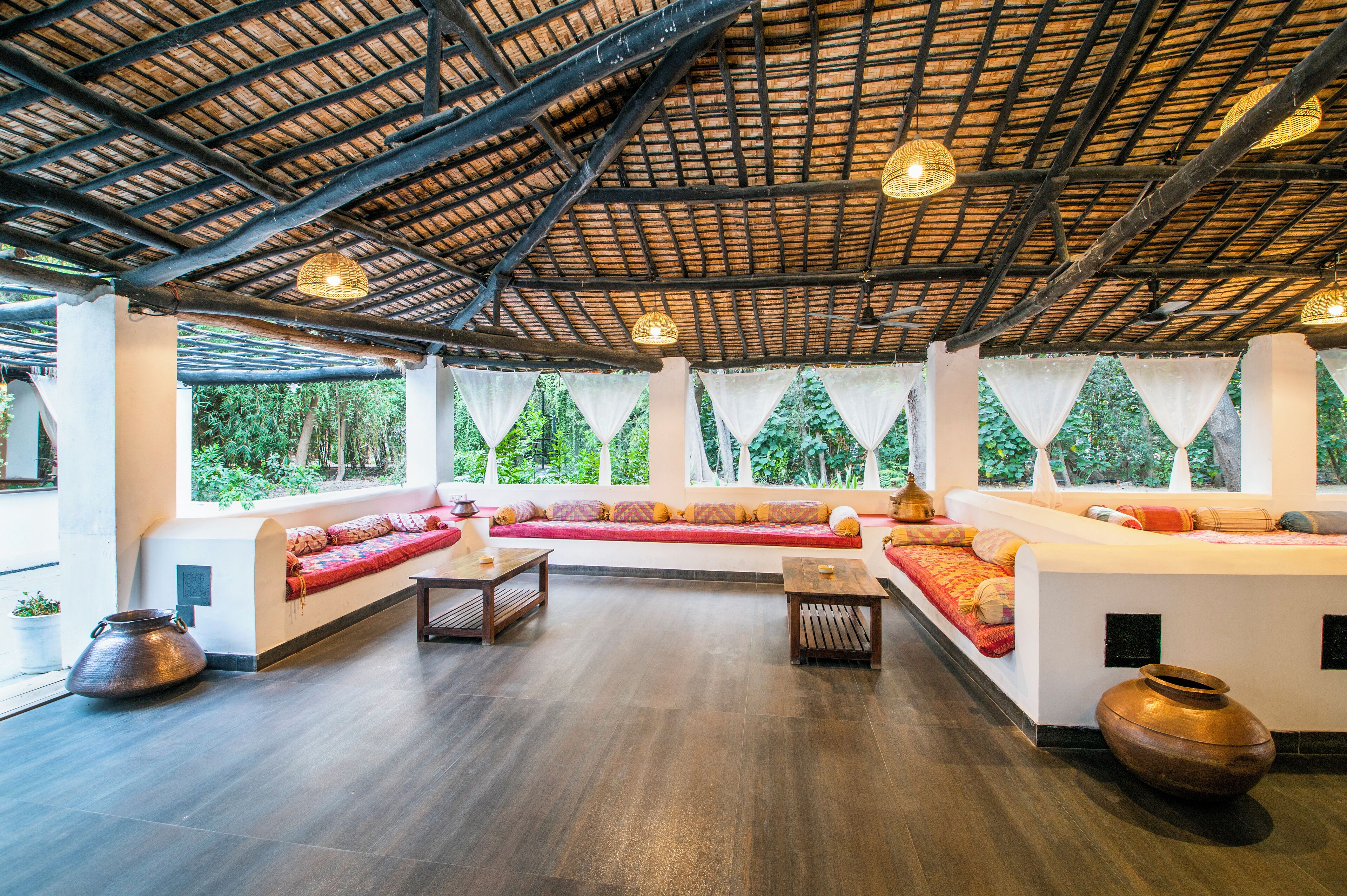 A spacious room with a high ceiling, large windows, and a seating area with cushions.