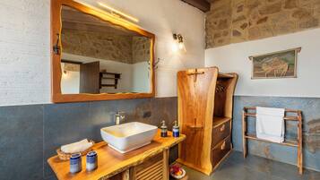 A bathroom with a stone wall, a wooden vanity, a large mirror, and a wooden shower enclosure.