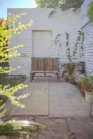 Een terras met een houten bankje, plantenpotten en een witte bakstenen muur.