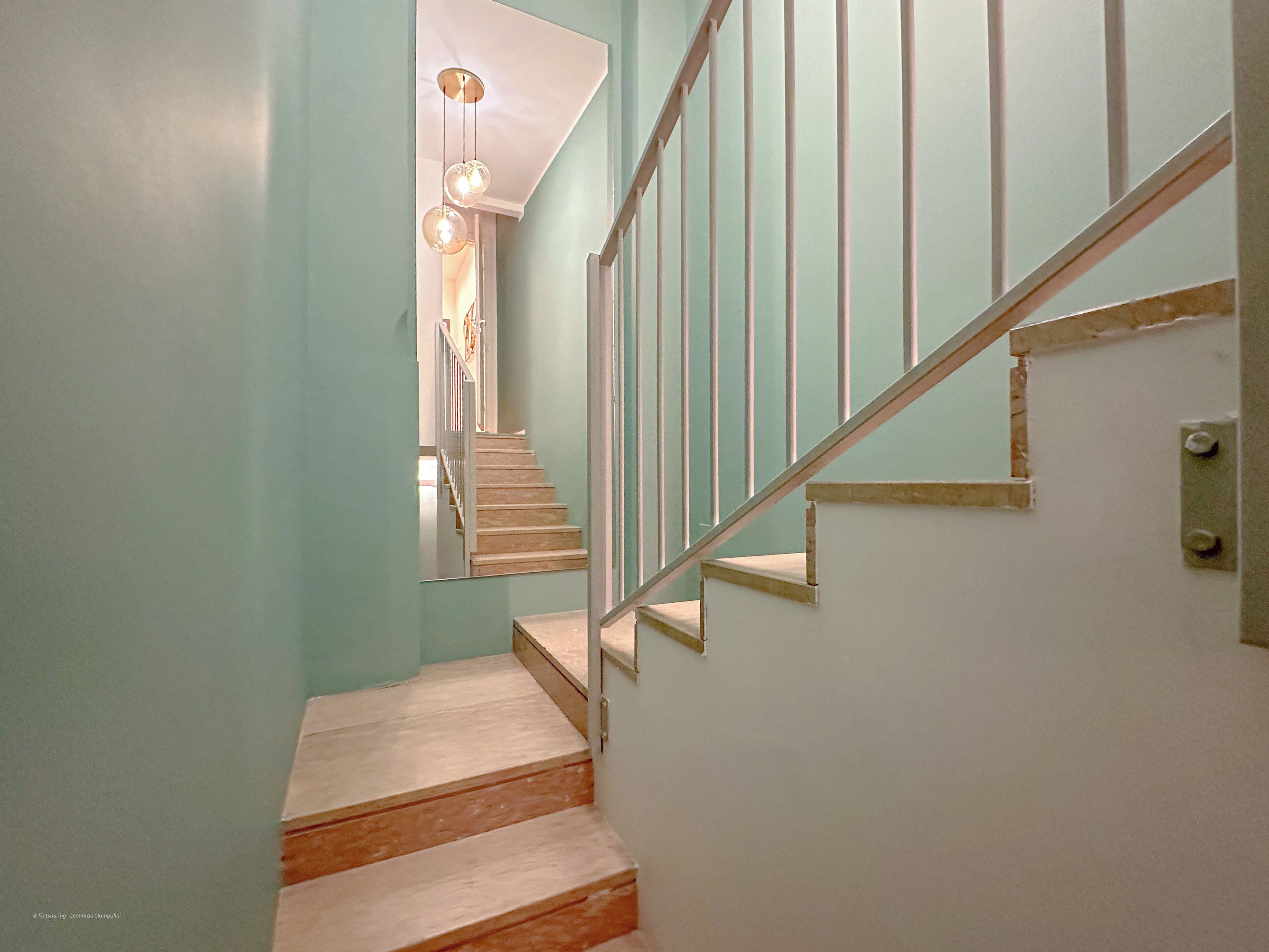 Eine Treppe mit Holzsitzen und Metallgeländern, die zu einer Zwischenebene mit einer Leuchte führt.