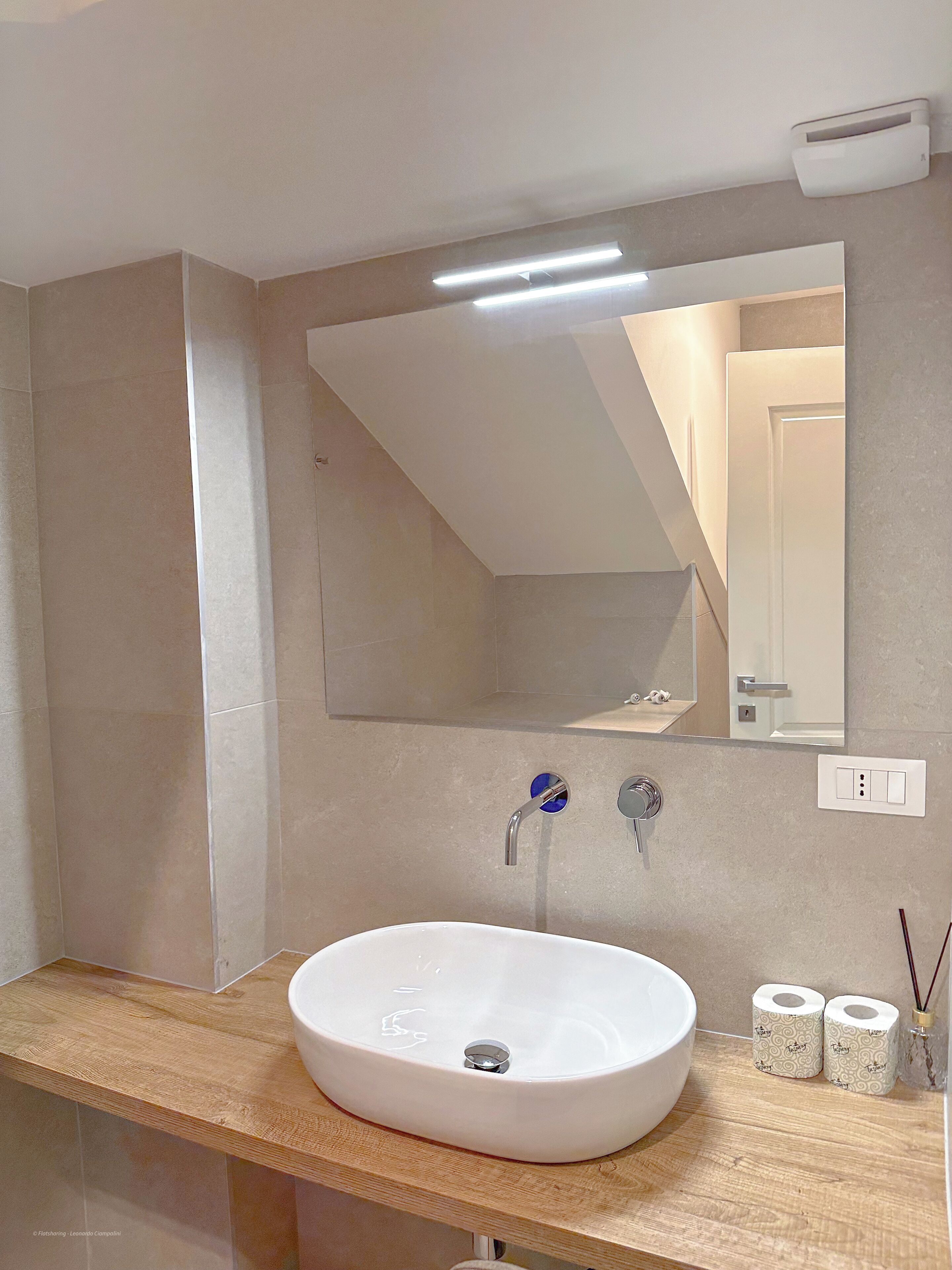 A modern bathroom with a large mirror, a white sink, and a wooden countertop.