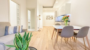 A modern living room with a sofa, a dining table with chairs, a potted plant, and a kitchen area in the background.