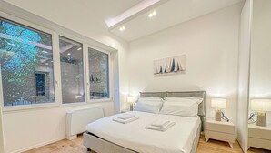 A bedroom with a large bed, two bedside tables with lamps, a window with a view of trees, and a painting on the wall.