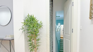 A hallway with a potted bamboo plant, a mirror, and a staircase leading to another room.