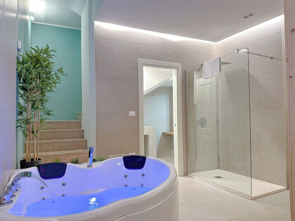 Une salle de bain moderne dotée d’une douche à parois de verre, d’une baignoire à jets et d’un escalier menant à un niveau supérieur.