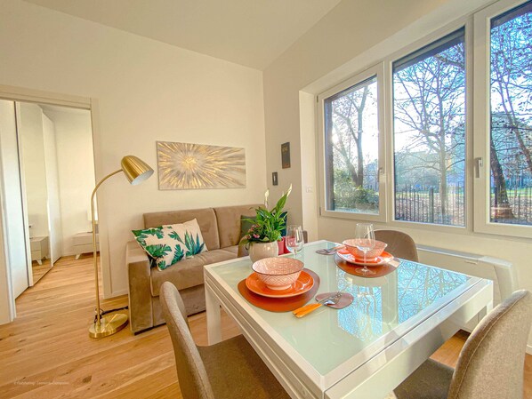 Un espace repas avec une table en verre, des chaises et une vue sur les arbres à travers de grandes fenêtres.