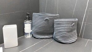 Une salle de bain avec un mur en marbre, un distributeur de savon pour les mains et le corps, et deux paniers en osier.