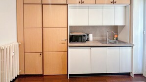 A compact kitchen with wooden cabinets, a microwave, a kettle, and a sink.