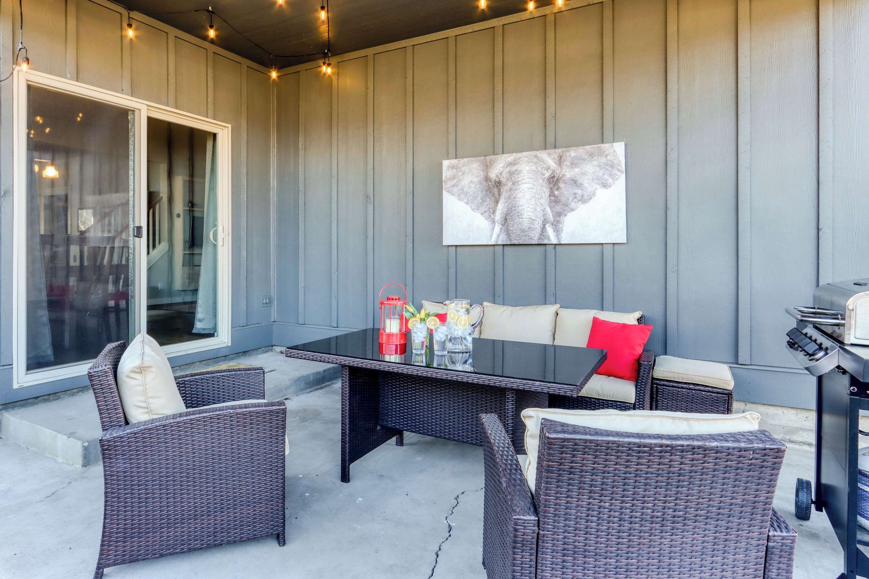 An outdoor patio with wicker furniture, a glass-top table, and a barbecue grill.