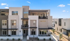 A modern multi-story residential building with balconies, large windows, and a clear sky.