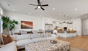 A spacious living room with a sofa, ottoman, and a dining area with a kitchen in the background.