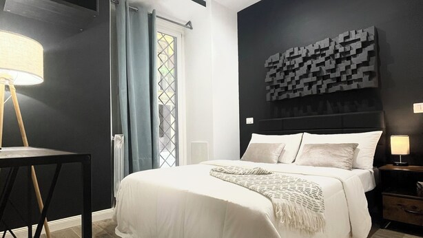 Een moderne slaapkamer met een groot bed, een bureau en een abstract kunstwerk aan de muur.