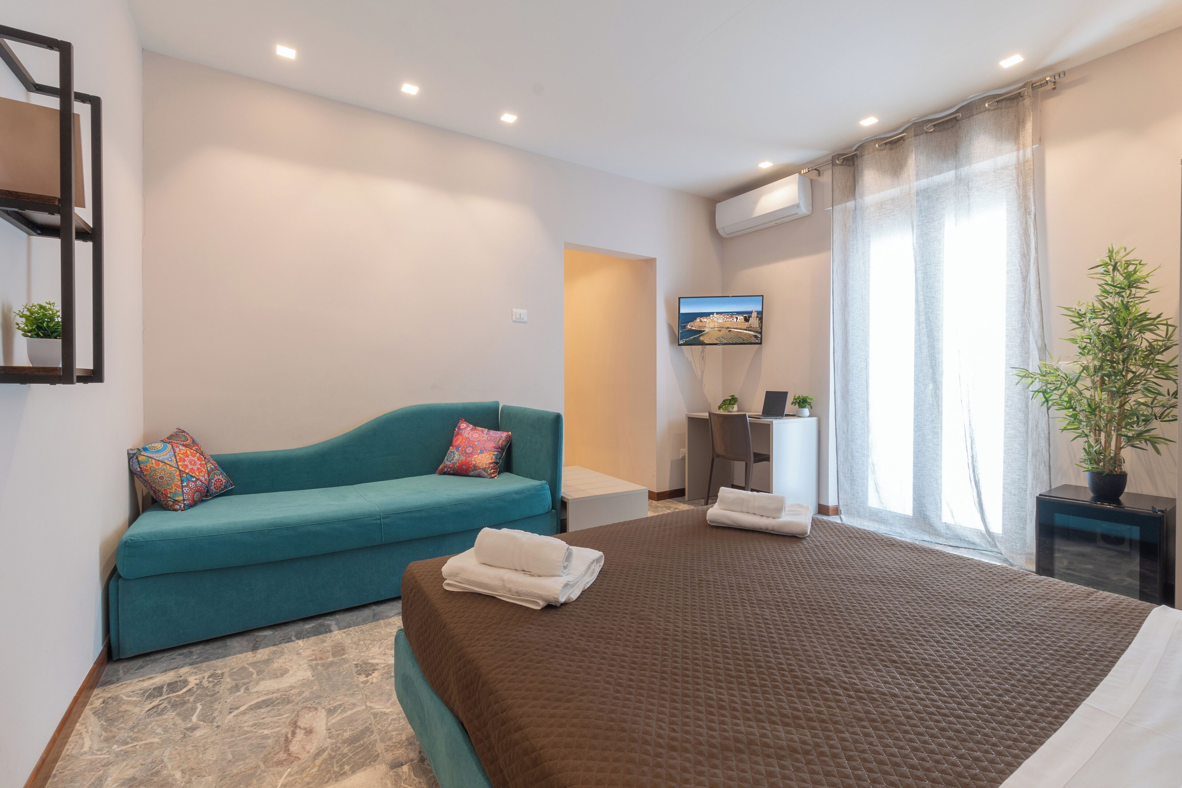 Habitación de hotel con cama, sofá, escritorio, televisor y ventana con cortinas.