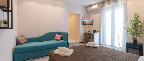 Habitación de hotel con cama, sofá, escritorio, televisor y ventana con cortinas.