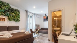 A modern hotel room with a bed, a desk, a seating area, and a bathroom. - Suebi Central - Deluxe Rooms & Family Suites (Termoli)