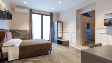 Une chambre d’hôtel moderne équipée d’un lit, d’un bureau, d’une chaise, d’une télévision et d’une salle de bain visible à travers une porte ouverte.