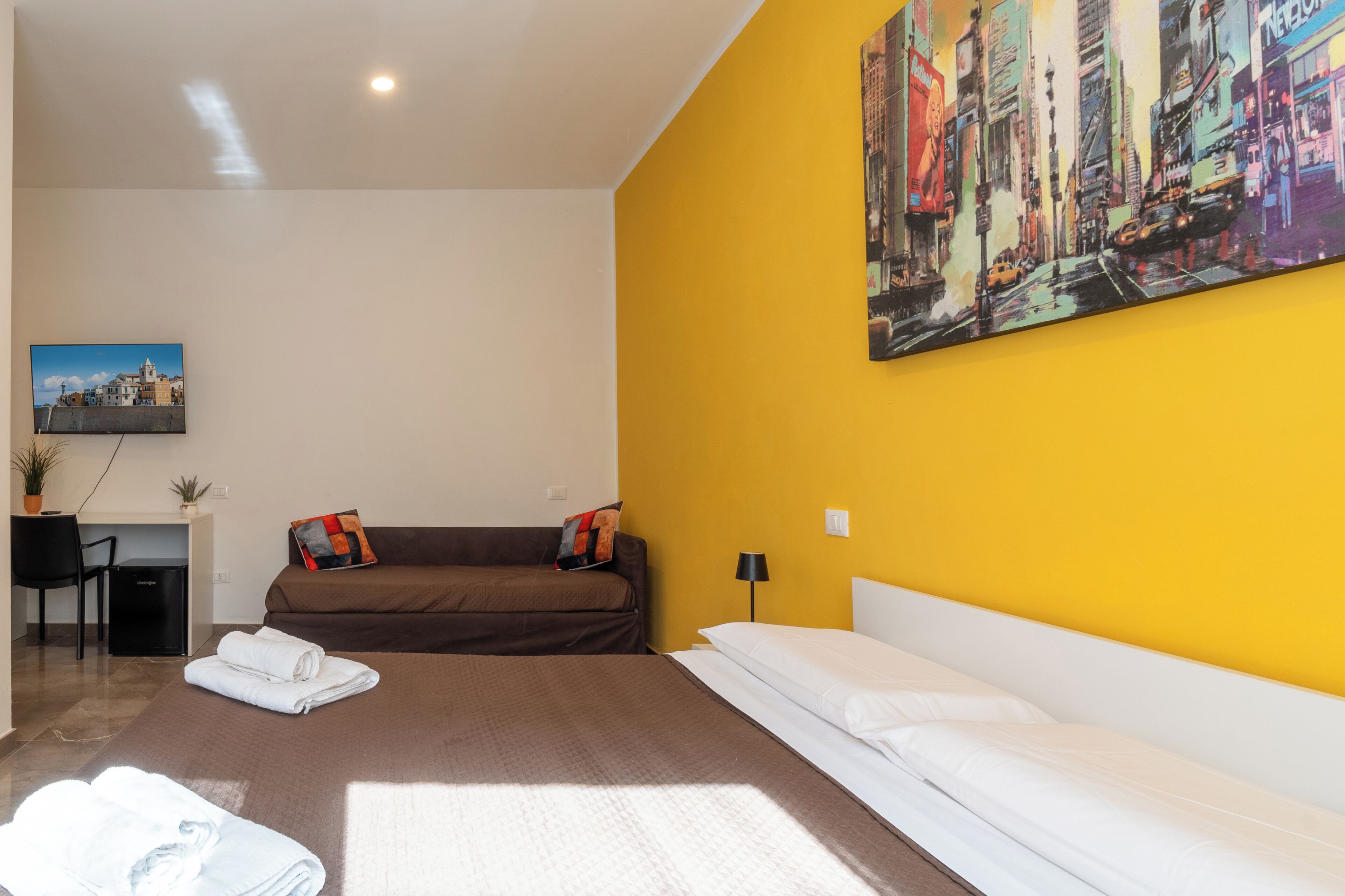 Una habitación de hotel con cama, sofá, escritorio y un cuadro en la pared.